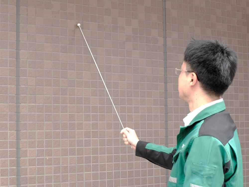 点検資格者が建物の外壁を打診器で検査している画像